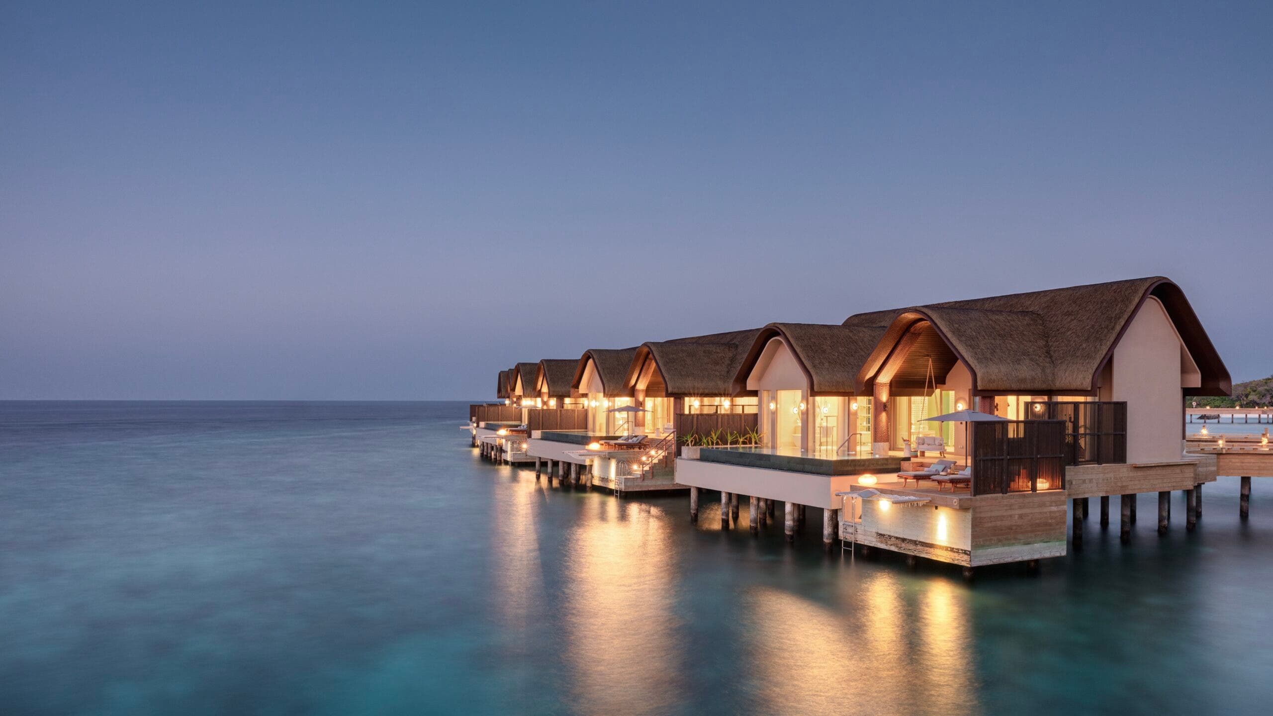 Image of over-water cabins at Joali Being in the Maldives. Light from inside the cabins illuminates the still blue water in the Indian Ocean
