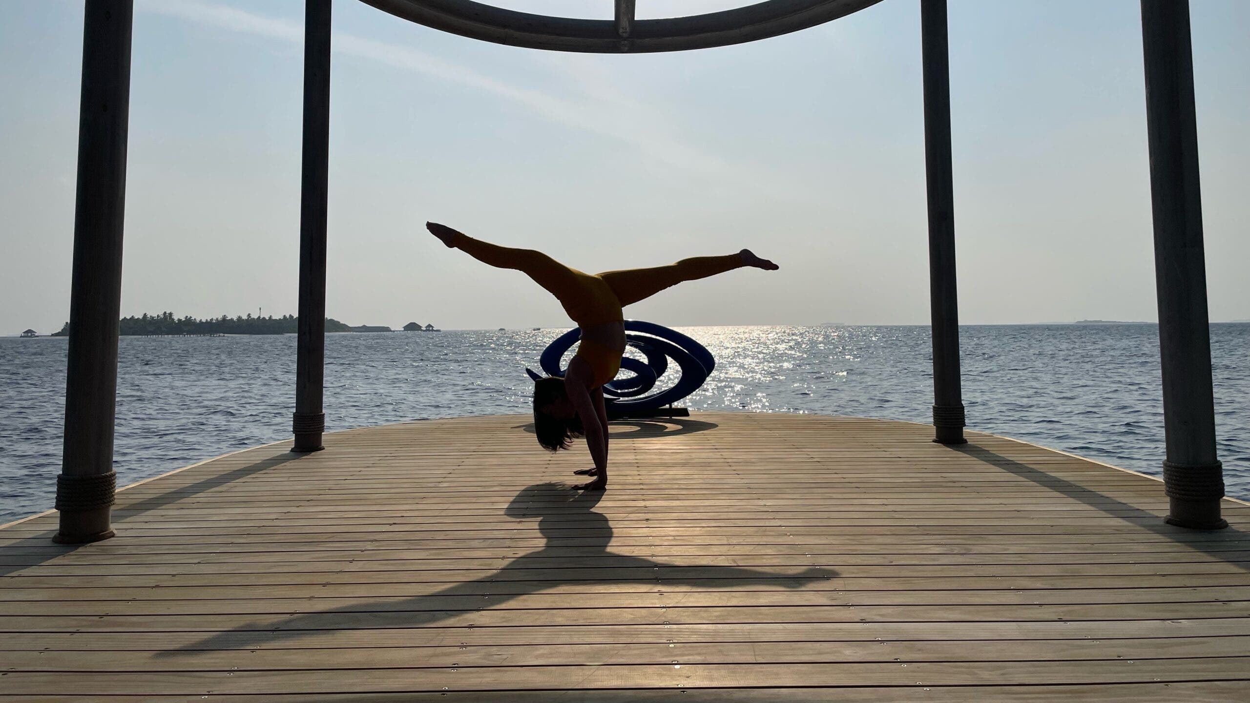 A person practices a handstand split on a dock over the ocean