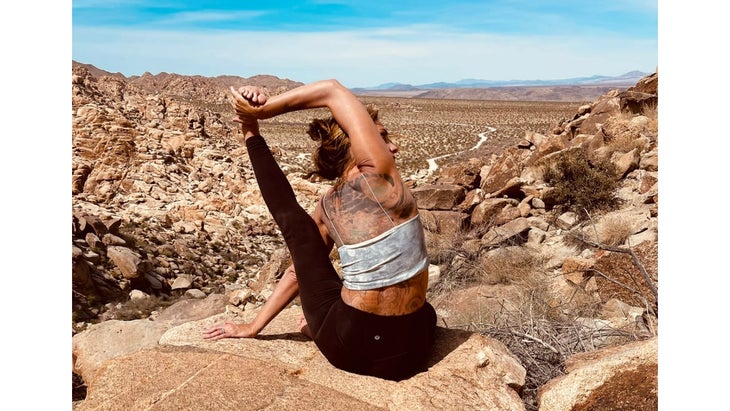 A woman practices Compass Pose in yoga on a rocky landscape 