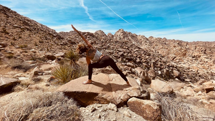 A woman practices Extended Side Angle outside on a rock