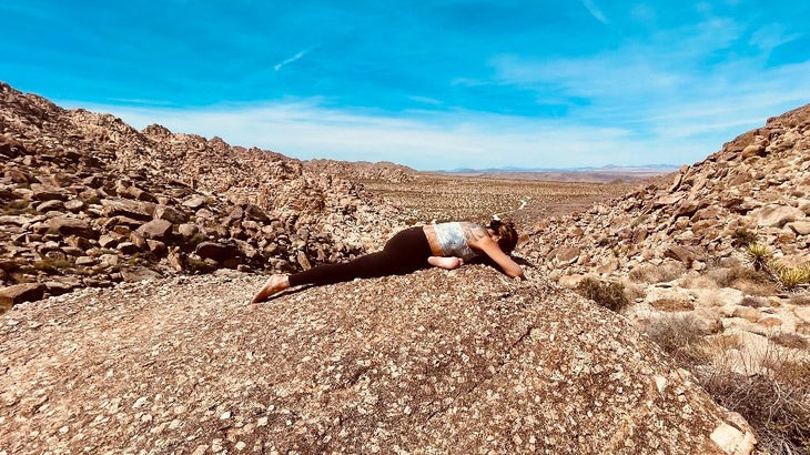 A woman practices One-Legged King Pigeon in yoga in a rocky landscape 