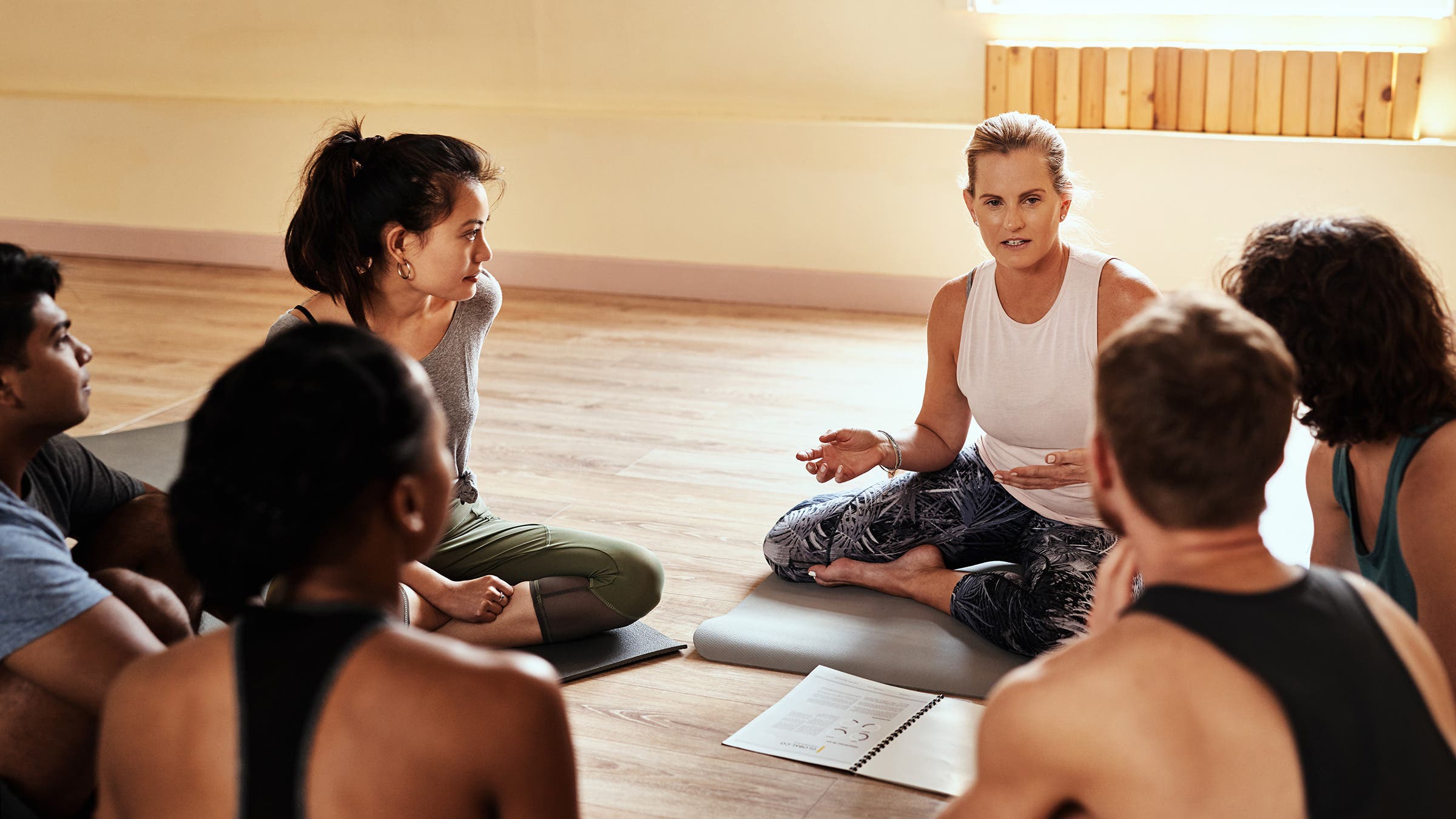 A group of people sit in a circle in a yoga studio during a yoga teacher training