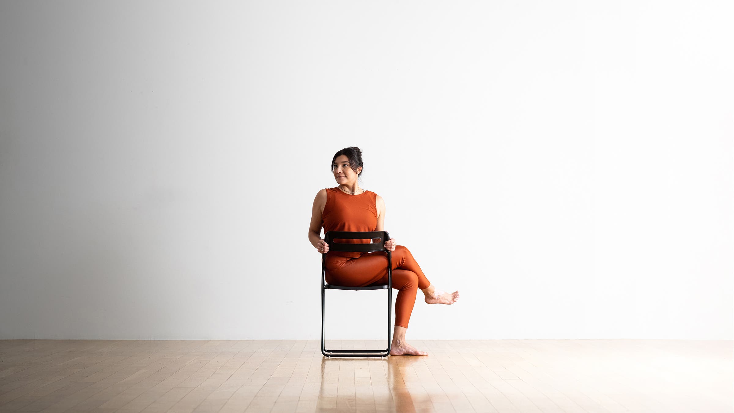 Dark haired woman practices Half Lord of the Fishes in a black chair.