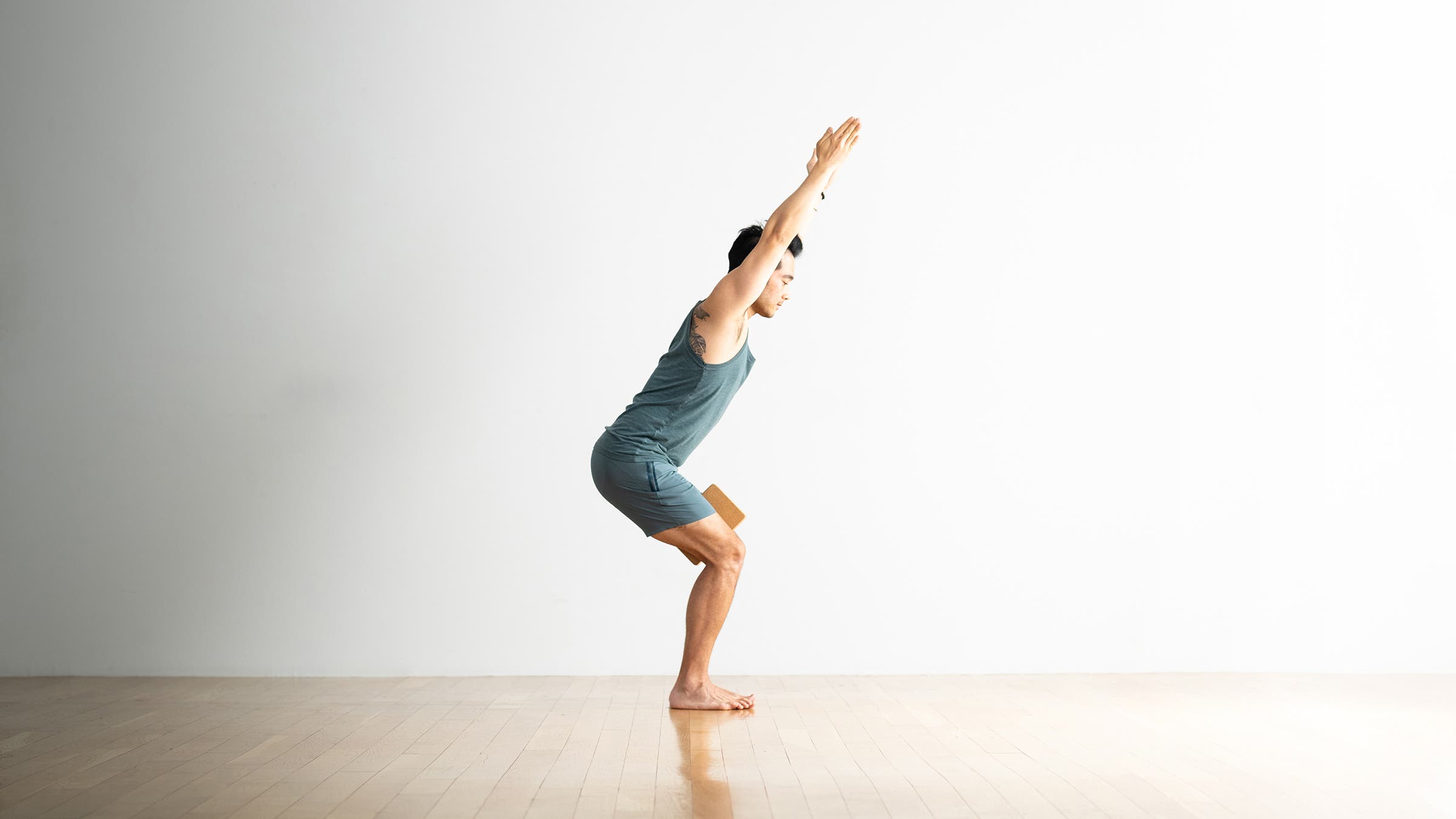 Hiro Landazuri practices chair pose with a cork block between his thighs, a yoga pose for leg strength