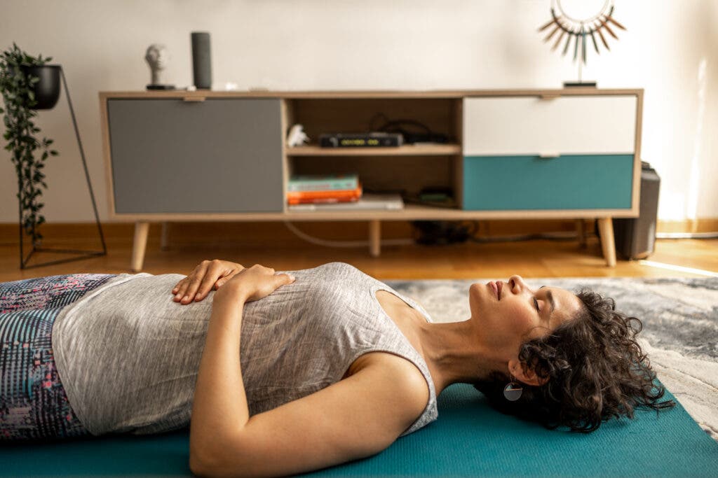 Woman lying on her back with hands on stomach and eyes closed.