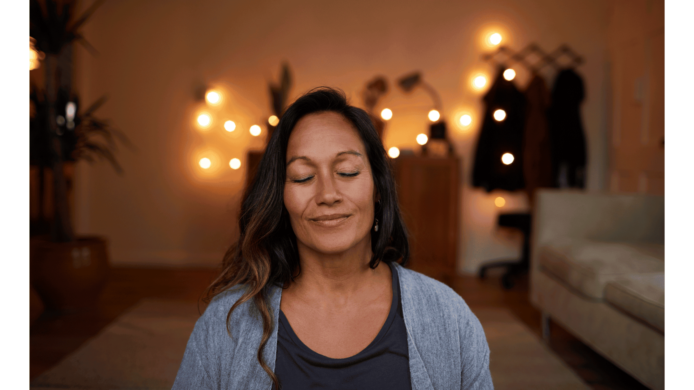 Woman sitting in a dimly lit room with her eyes closed practicing winter solstice rituals