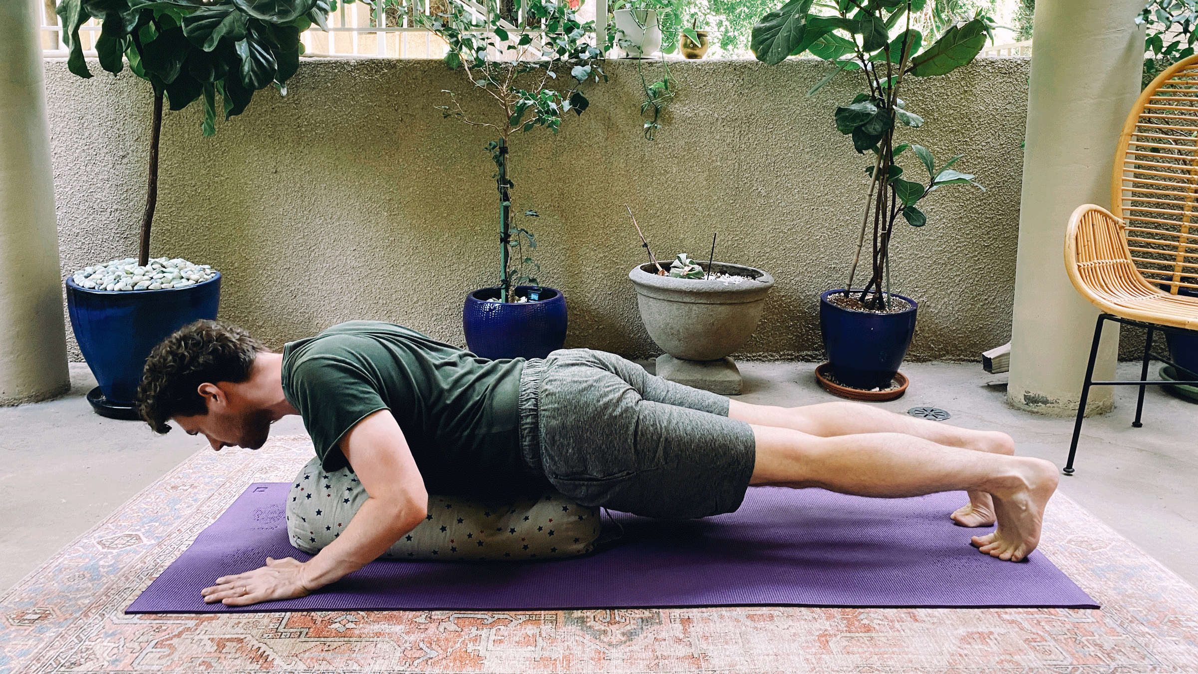 Man on his yoga mat practicing Chaturanga, or a half push-up, with a bolster beneath his chest