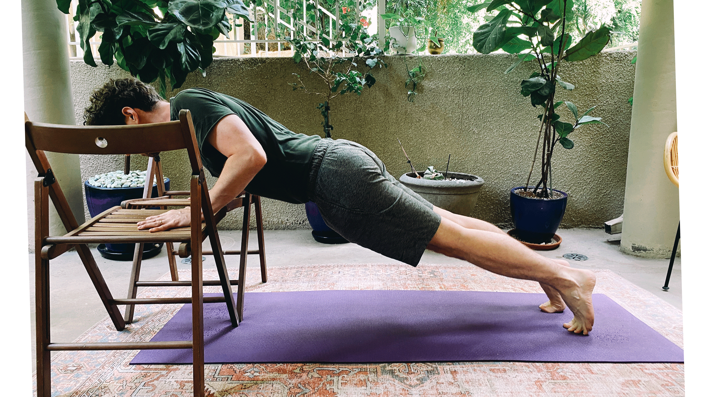 Man practicing Chaturanga, or a half push-up, with his hands on two chairs on his yoga mat