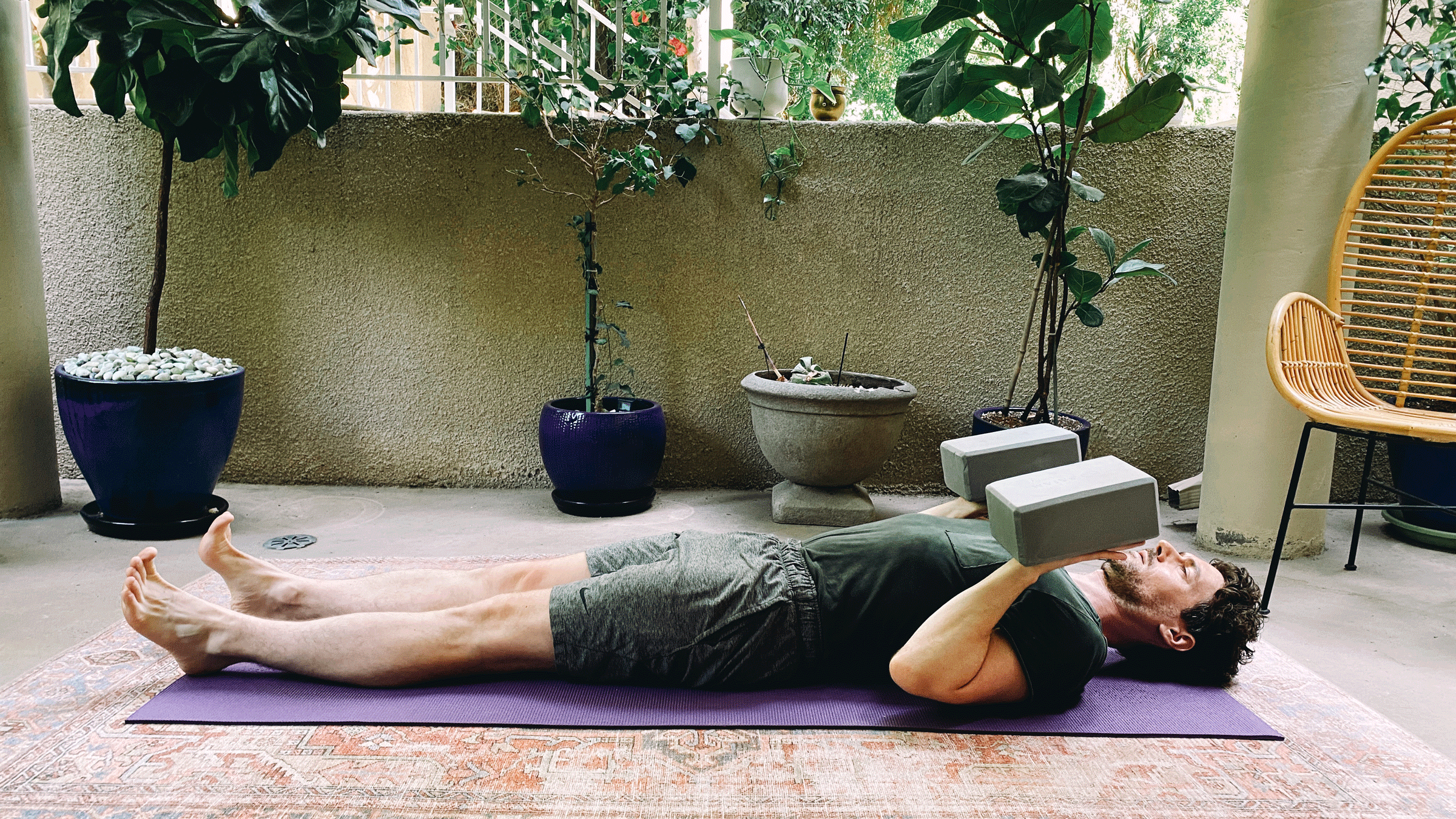 May lying on his back on a yoga mat with his elbows bent and foam blocks balancing on his hands in a variation of Chaturanga