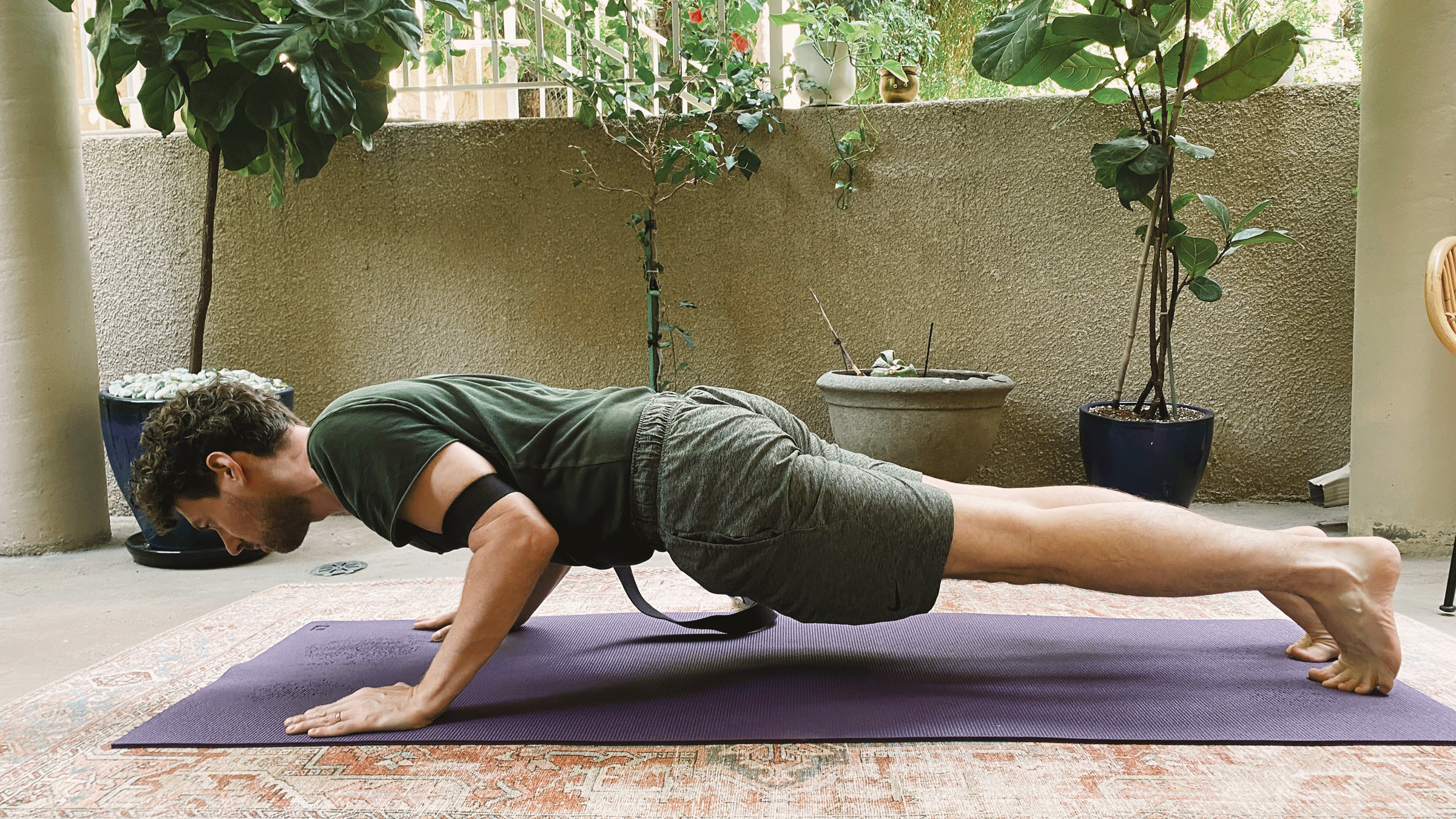 Man practicing Chaturanga, or a half push-up, with a strap around his upper arms