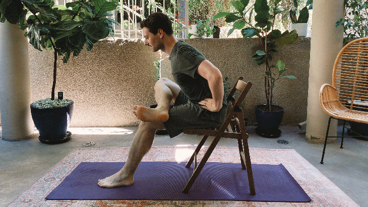 Man sitting on a chair with his right ankle to his left thigh in a seated version of Pigeon Pose