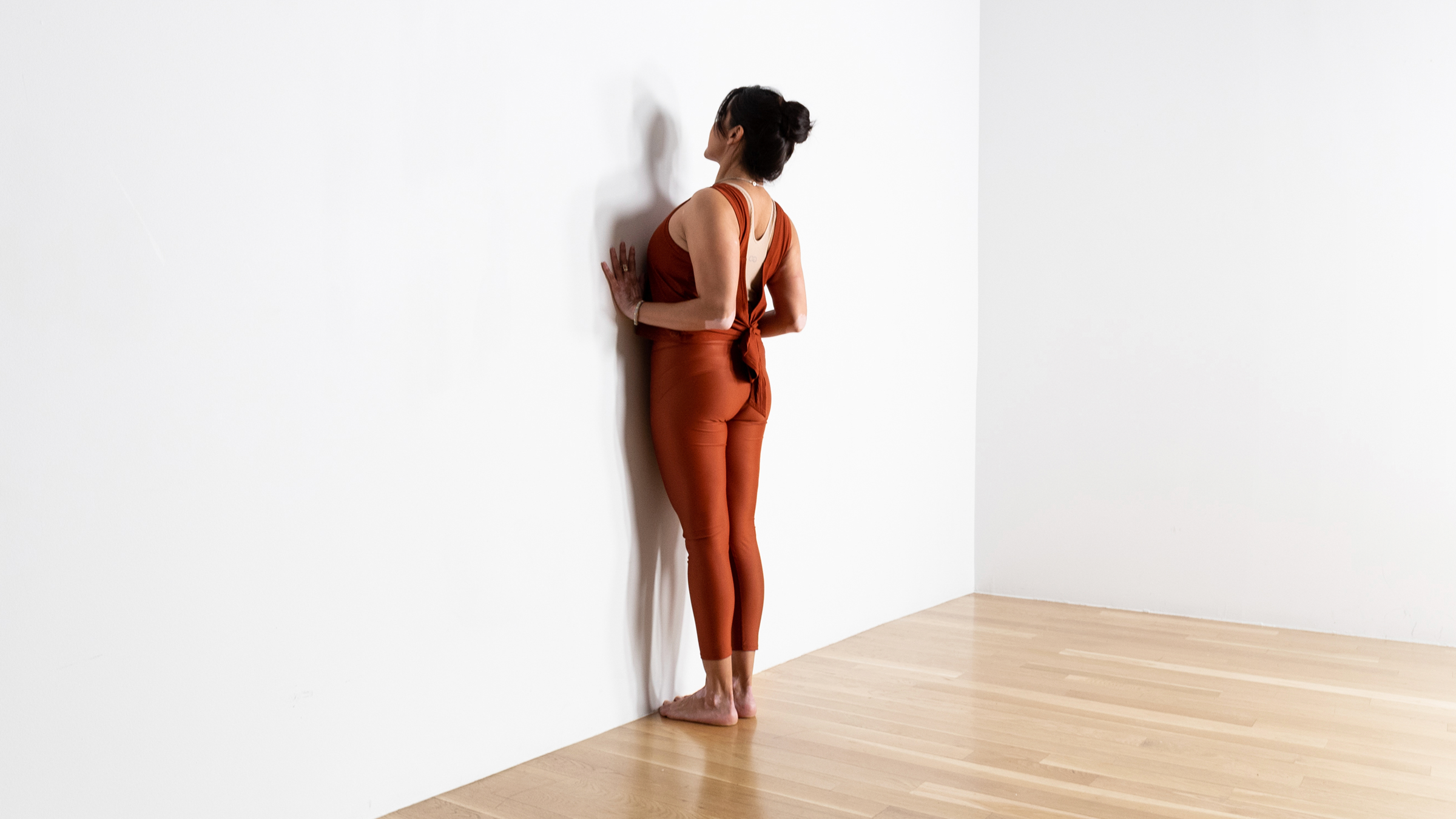 A woman with dark hair practices Cobra against the wall.Her hands are on the eall and shfe's