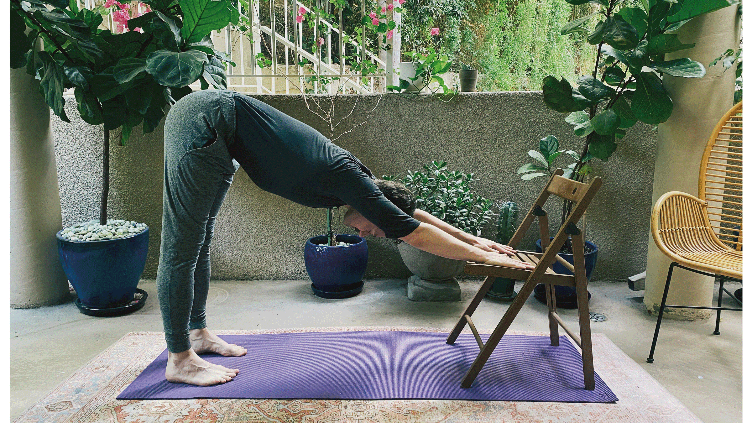 Man standing on a yoga mat with his feet hip-distance apart and his arms resting on the seat of a chair to form a V shape with his body