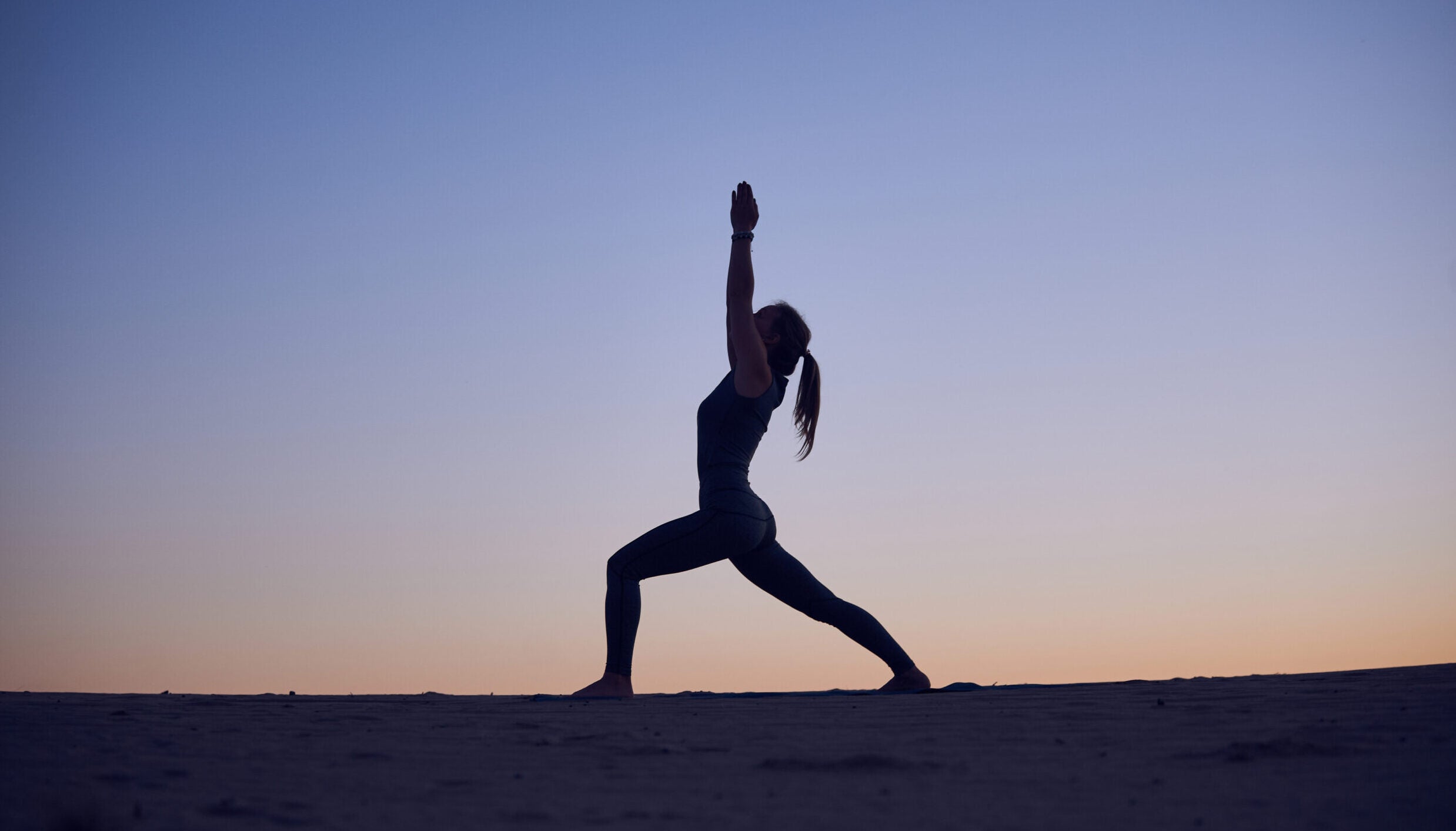 Woman practicing yoga outside beneath the full Moon in Aries in Warrior 1 yoga pose