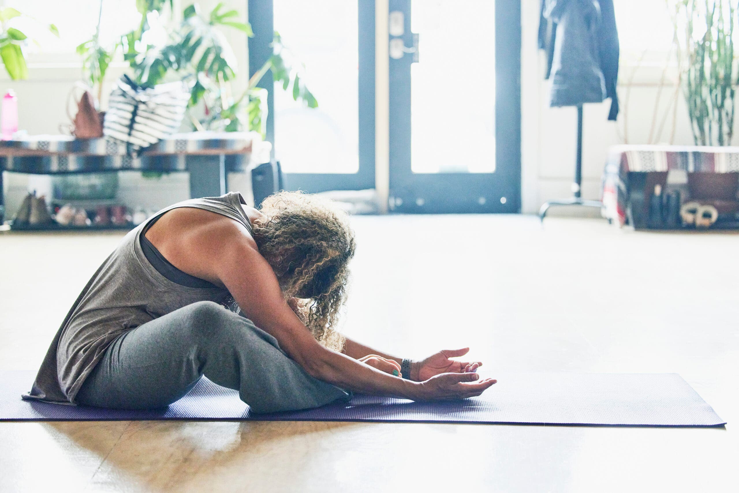 Woman on her yoga mat with bent knees falling out toward the sides and her upper body leaning over her thighs and her shoulders relaxed