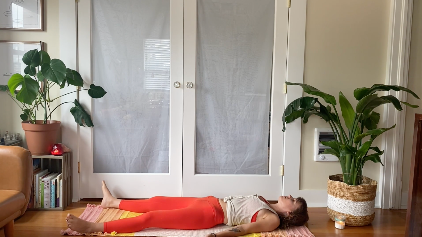 Woman lying on her yoga mat in Savasana with plants in the background