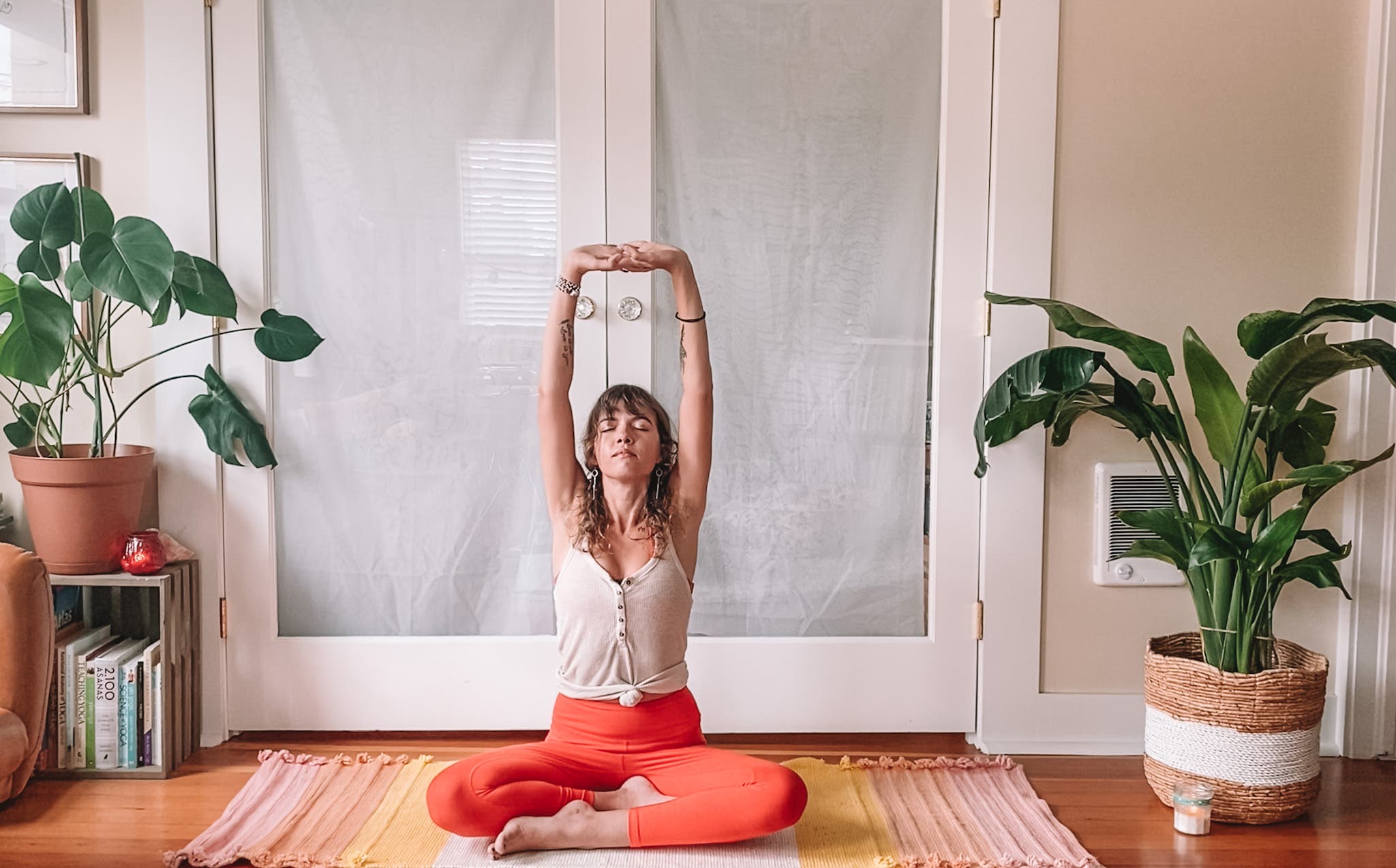 Woman seated cross-legged on her yoga mat with her fingers interlaced and arms reaching upward during the Full Moon in Aries