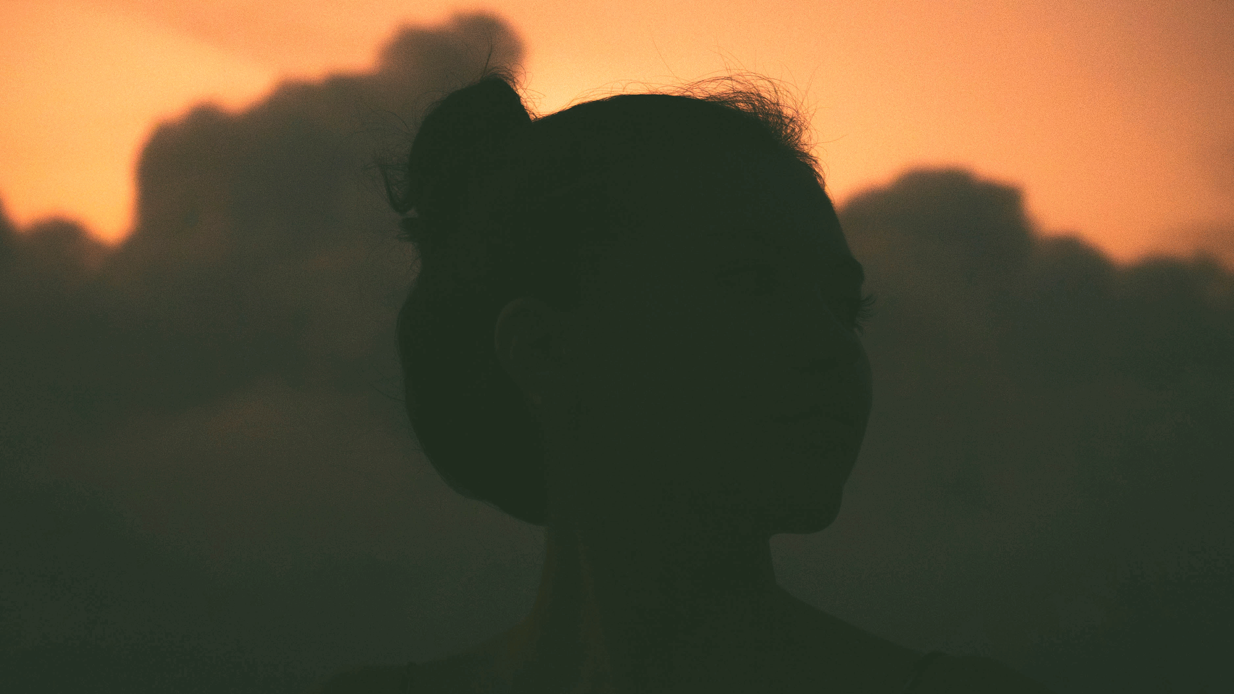 Woman standing outside at sunset with clouds on the horizon pondering the weekly astrology forecast