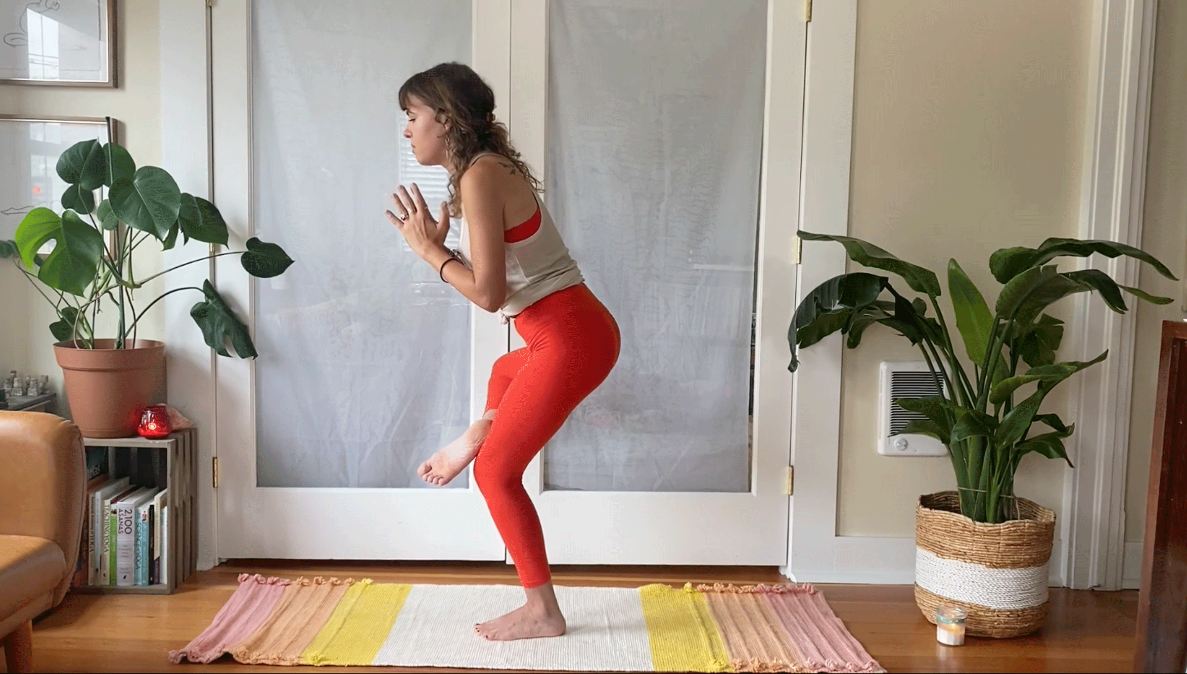 Woman balancing on one leg on her yoga mat with her right ankle on her left thigh and her hands in prayer at her heart