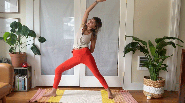 Woman on her yoga mat leaning to the side in Reverse Warrior Pose in yoga