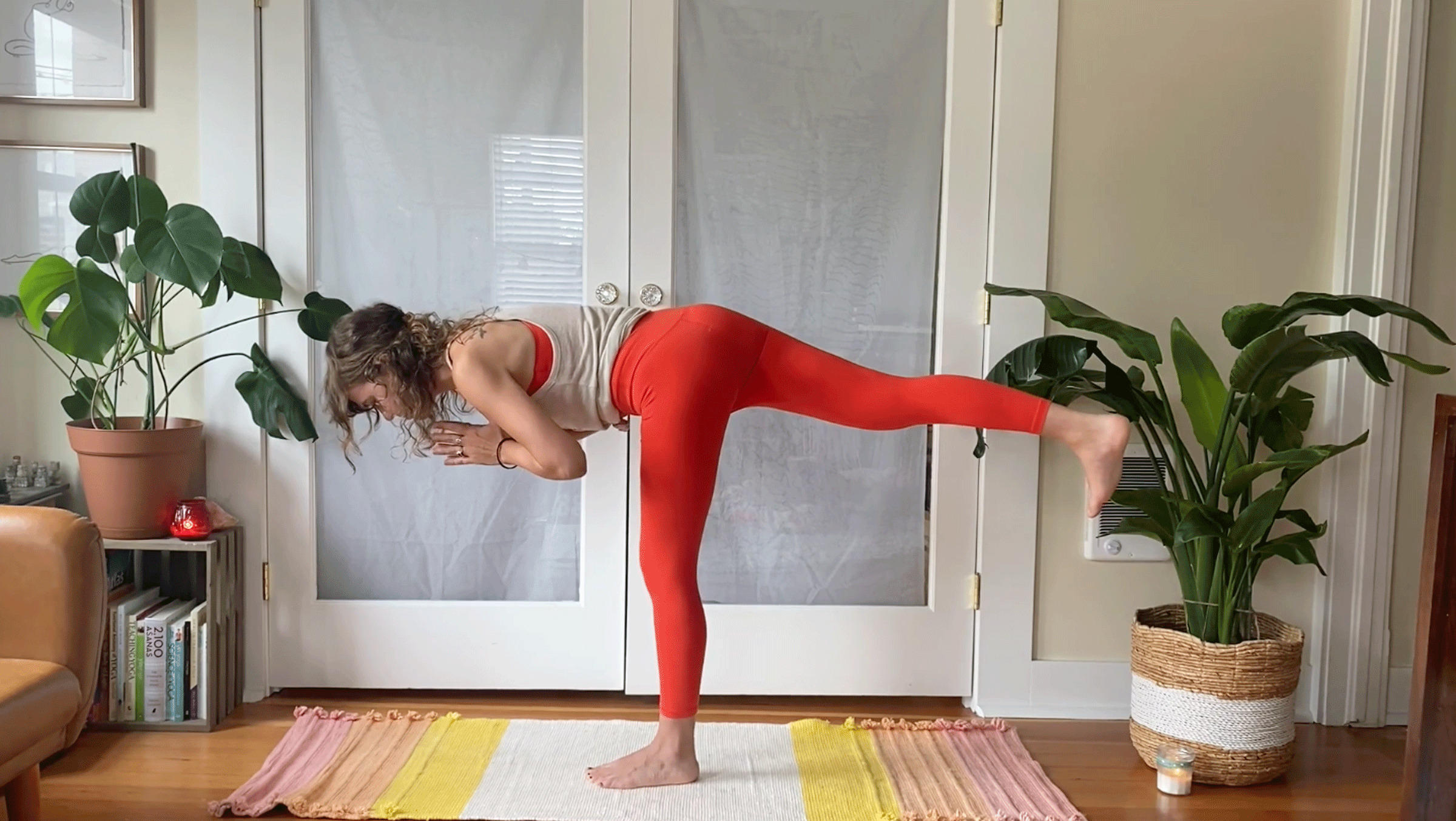 Woman balancing on one leg on her yoga mat with her right leg extended parallel to the floor and her hands at her heart in prayer