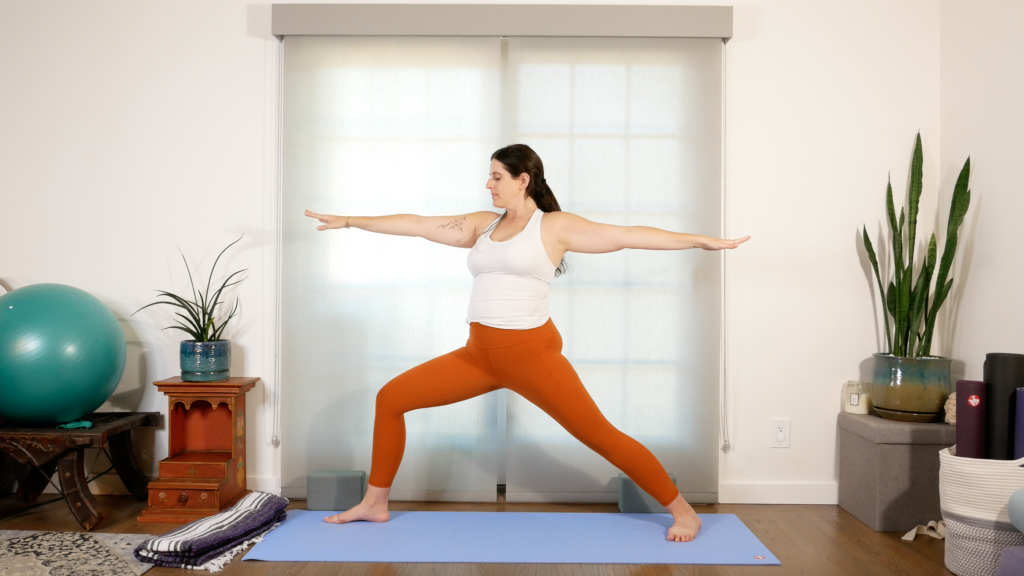 Woman standing on her yoga mat in Warrior 2 Pose with her arms alongside her ears