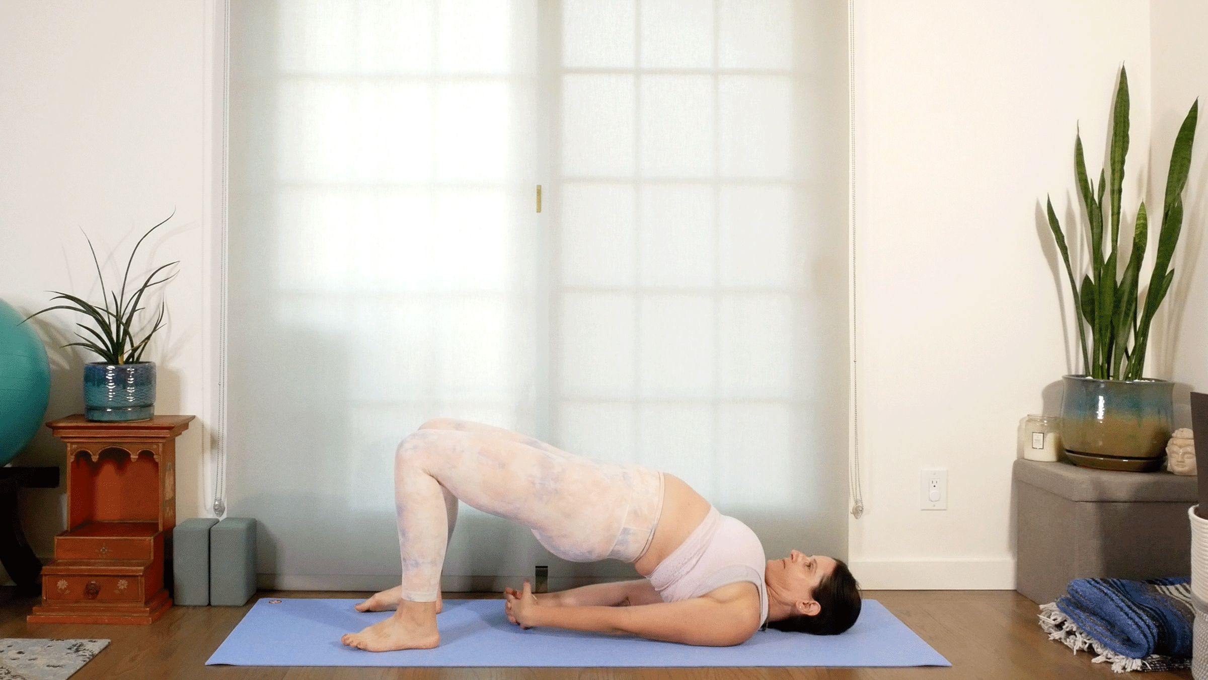 Woman lying on yoga mat practicing Bridge Pose with her hands clasped behind her back