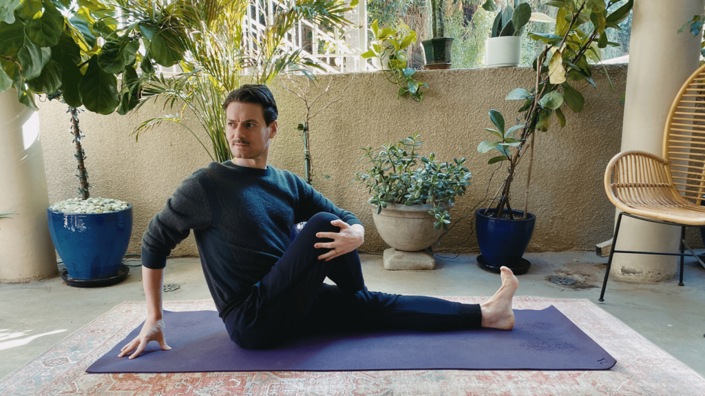 Man sitting on a yoga mat with his right foot crossed over his left knee and his chest twisting to the right in Half Lord of the Fishes