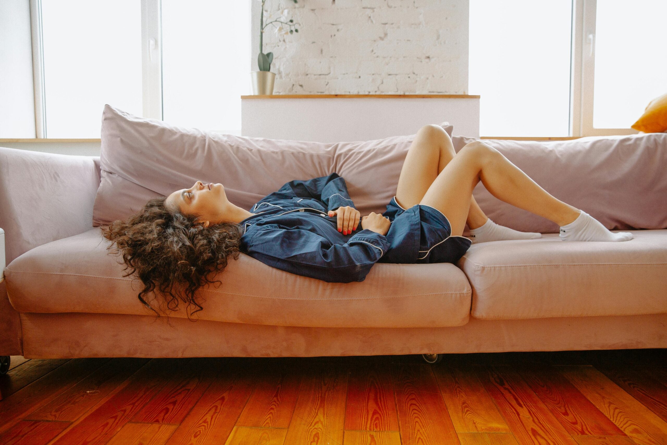 Woman lying on couch gripping her stomach with both hands.