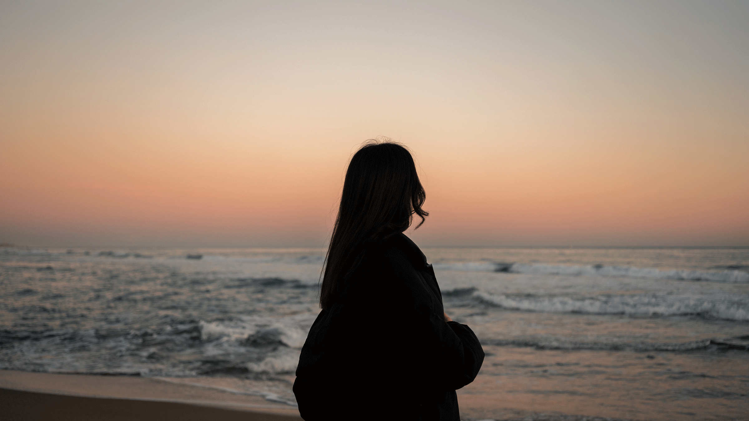 Woman standing at the beach washing the waves lap onto sand as she contemplates the new Moon in Pisces