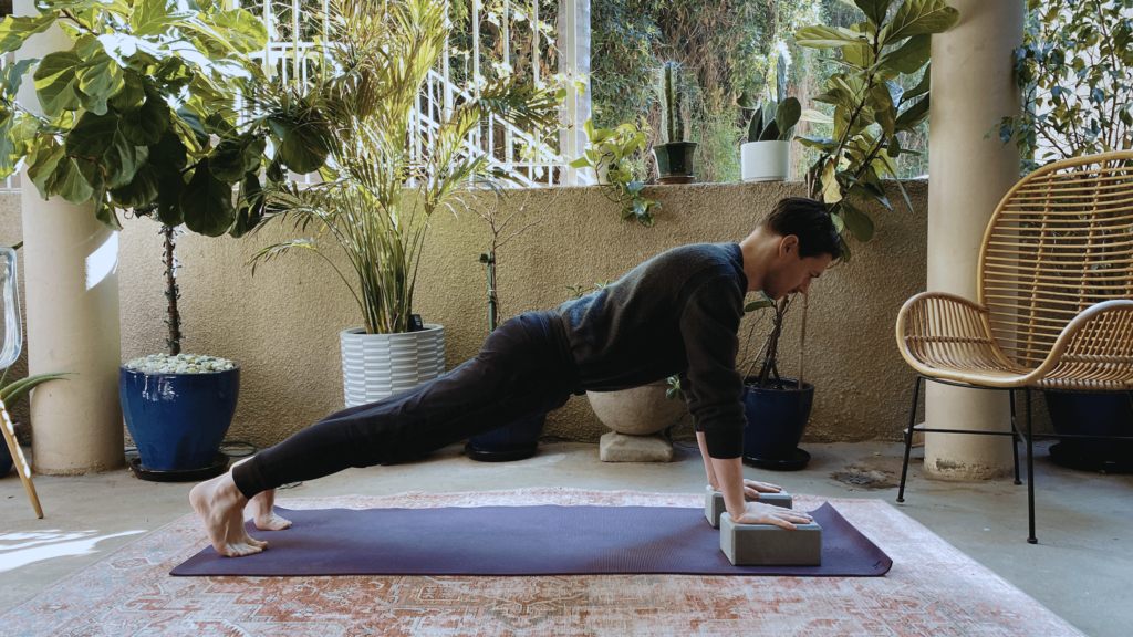 Man on a yoga mat with a block beneath each hand practicing Plank Pose