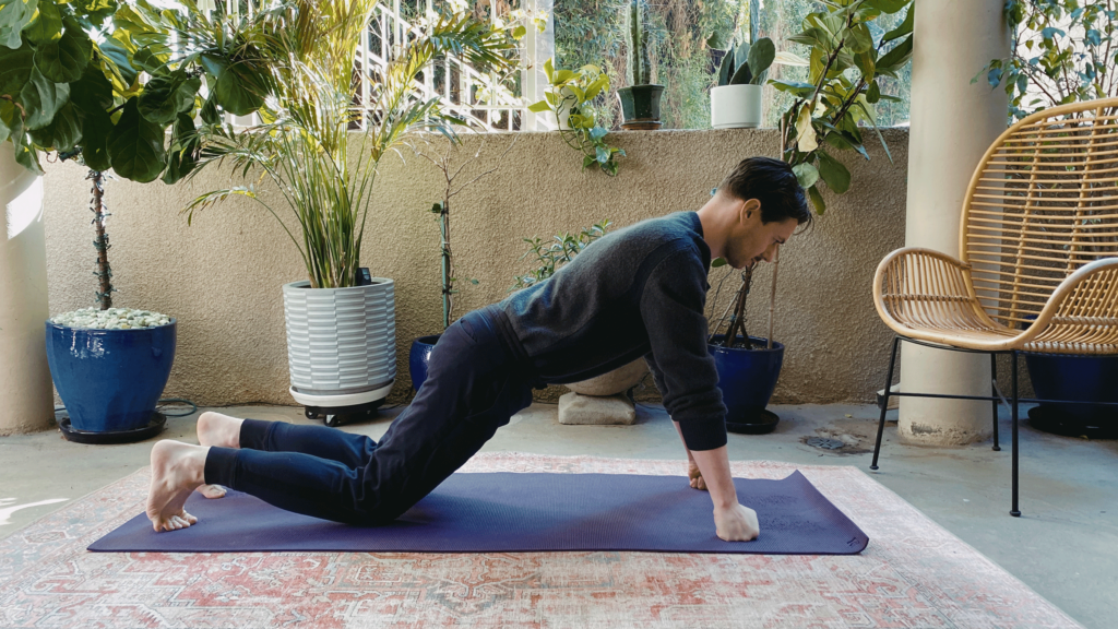 Man on a yoga mat with his knees down and his hands in fists in Plank Pose