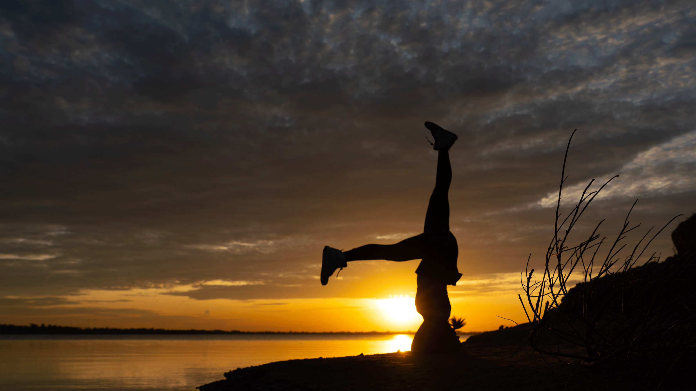 Woman outside at night standing on her head with the sunset and the mountains in the backdrop