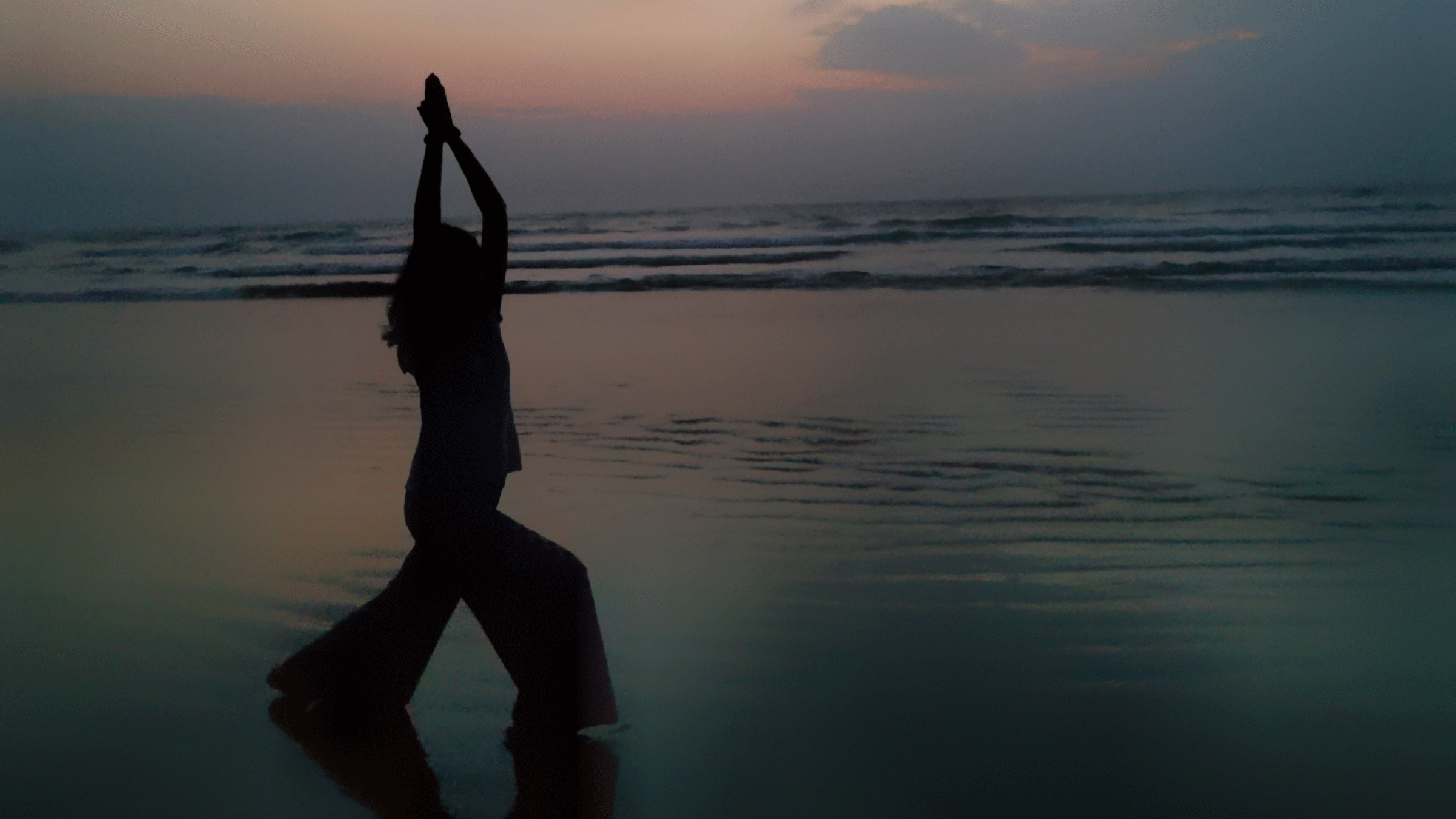 Woman standing on a beach at sunset practicing yoga and meditation while contemplating astrology