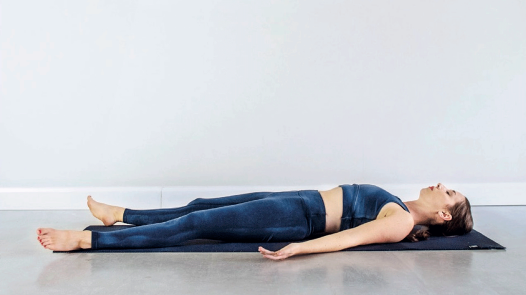 Kassandra Reinhardt lying on her back on a yoga mat in Corpse Pose while practicing new Moon Yin Yoga