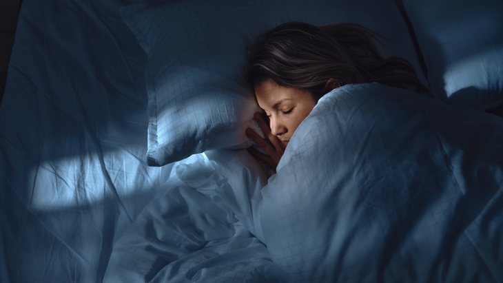 Woman who can fall asleep easily curled up in bed beneath a comforter