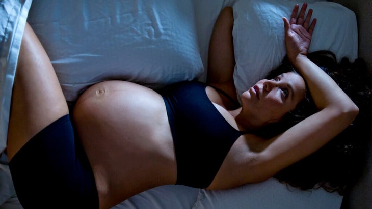 Pregnant woman lying in bed awake at night because she's too hot to sleep