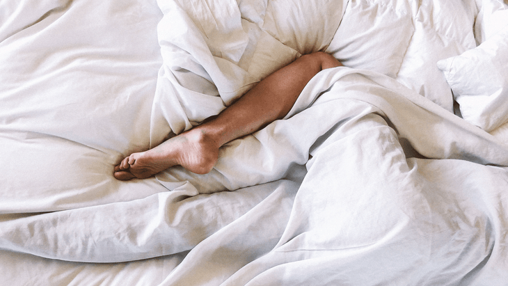Una mujer acostada en la cama con las piernas fuera de debajo de la funda nórdica.