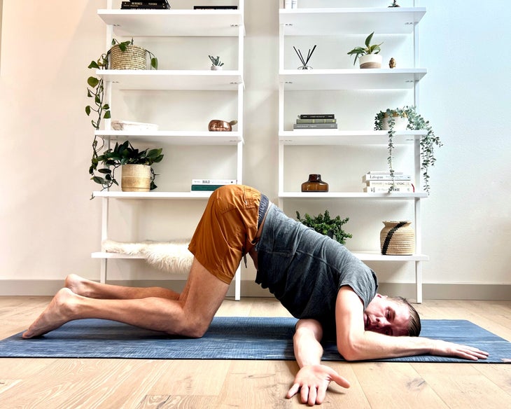 Man wearing a gray T-shirt and orange shorts practices yoga: Thread-the-Needle Pose