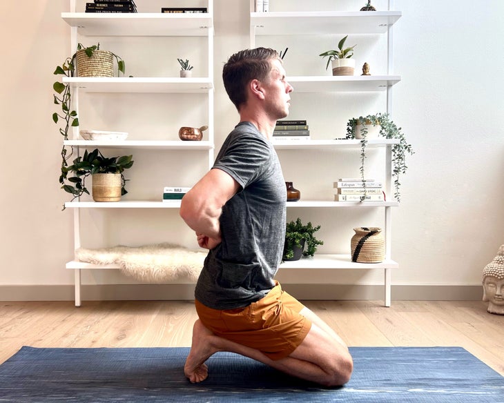 Man in gray shirt and orange shorts practices Pascim Namaskarasana (Reverse Prayer Pose)