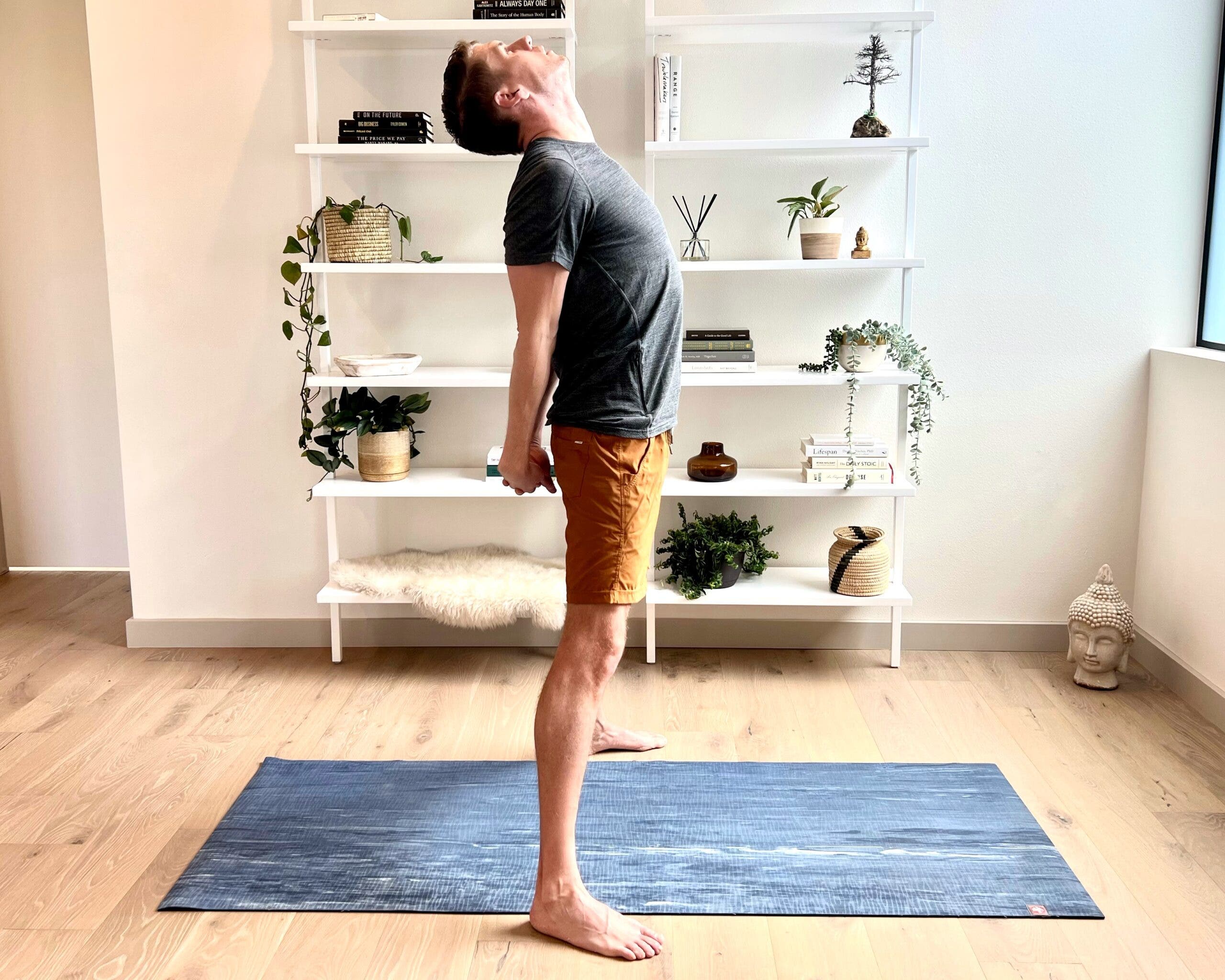 A man in a gray T-shirt and orange shorts practices Prasarita Padottanasana C (Wide-Legged Forward Bend), variation