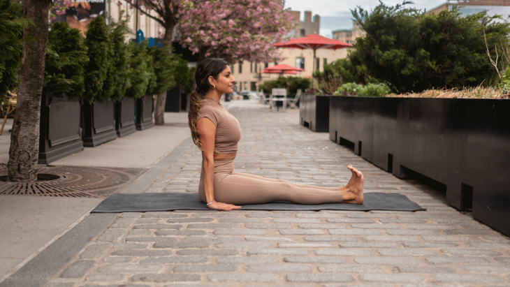 Woman sitting on her yoga mat with her legs extended straight in front of her in Staff Pose.