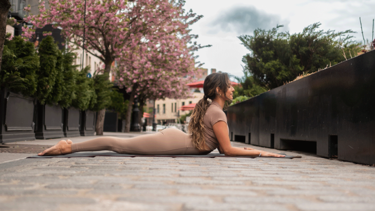 Woman lying on a yoga mat outside with a blossoming tree practicing Sphinx Pose