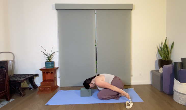 Dark-haired woman practicing Balasana with her head on a yoga block.