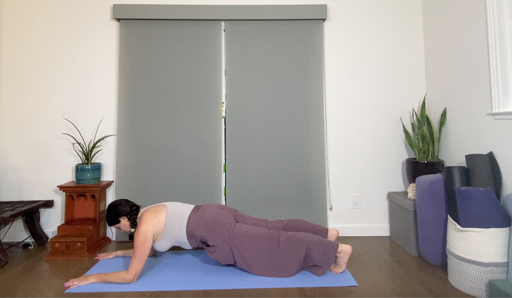 A dark-haired woman practices a forearm plank