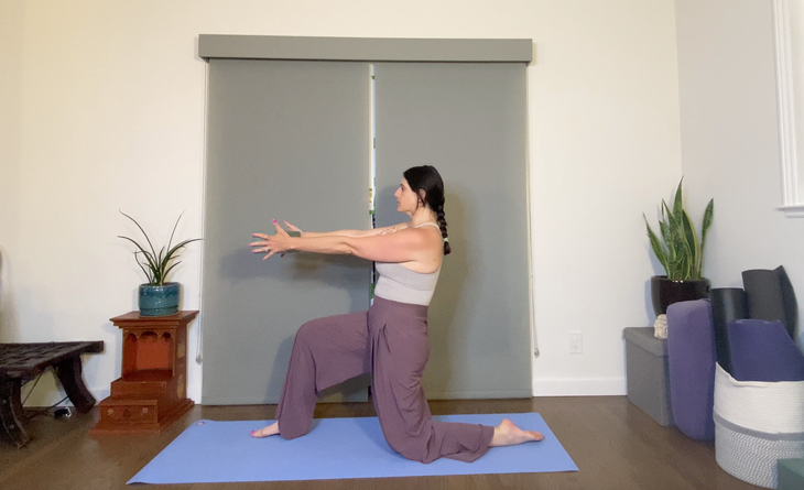 A woman with dark hair wearing purple pants kneels on a yoga mat doing a variation of Low Lunge holding a yoga block in front of her