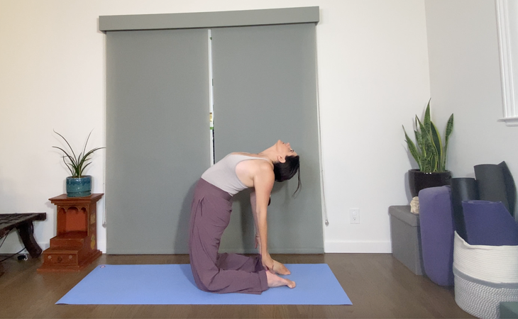 A woman with dark hair practices Camel Pose/Ustrasana.