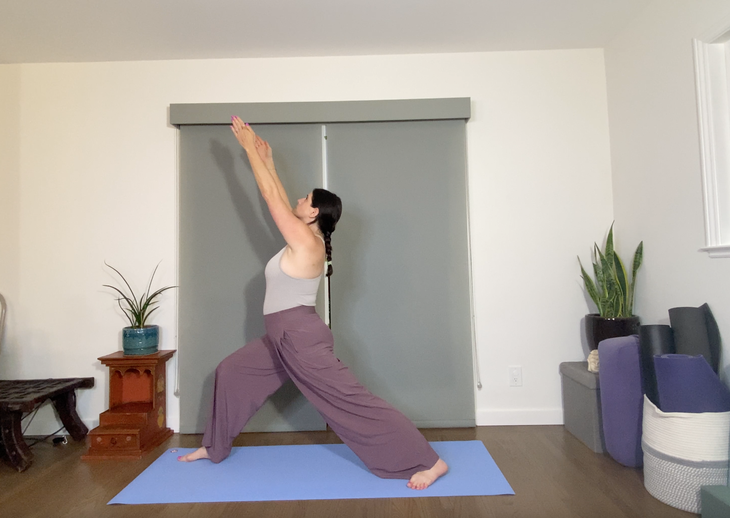 Woman in purpole pants practices a variation of Warrior I pose with her arms up