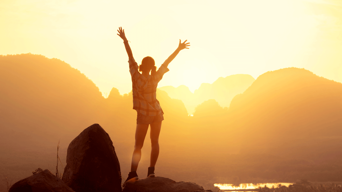 Woman hiker watching sunrise over the mountains with her arms thrown in the air
