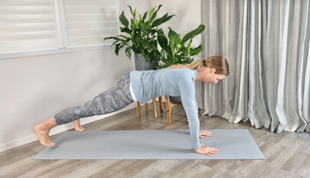 woman practicing plank pose on a yoga mat with legs wide.